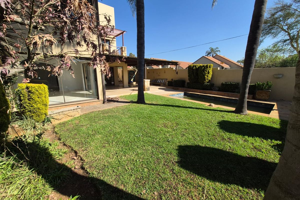 Rear garden featuring a swimming pool, covered patio area, and established trees, providing a private outdoor space for relaxation and entertainment.