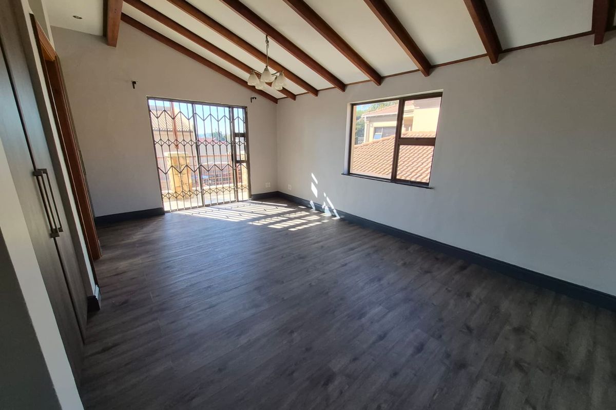 Spacious bedroom featuring vaulted ceilings with exposed timber beams, dark wood-look flooring, and a security gate leading to a balcony.