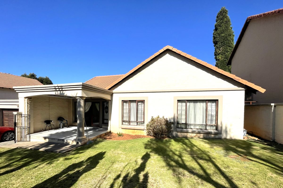 Rear view of the house featuring a covered patio with concrete columns, a well-maintained lawn, and a tiled roof.