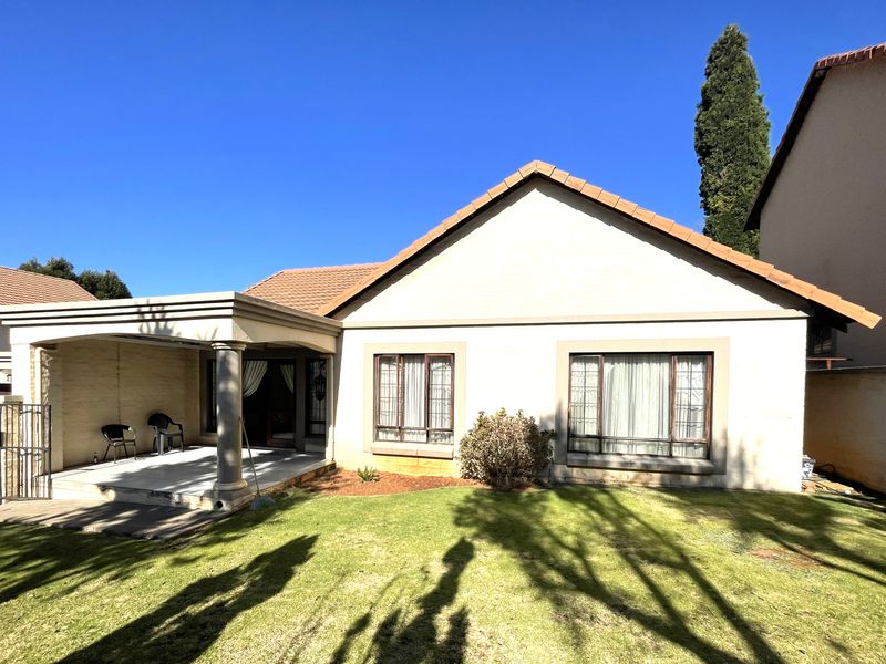 Rear view of the house featuring a covered patio with concrete columns, a well-maintained lawn, and a tiled roof.