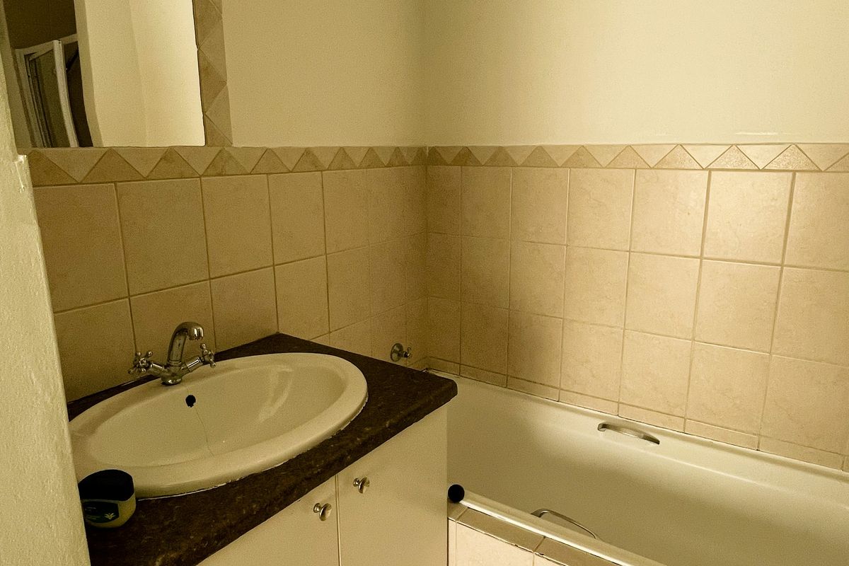 A functional bathroom featuring a vanity cabinet with a drop-in basin, a bathtub, and neutral wall tiling.