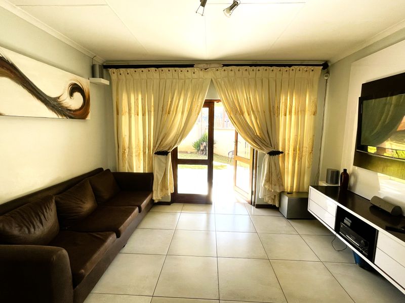 A living room featuring tiled flooring and a glass panel door providing direct access to the rear garden area.