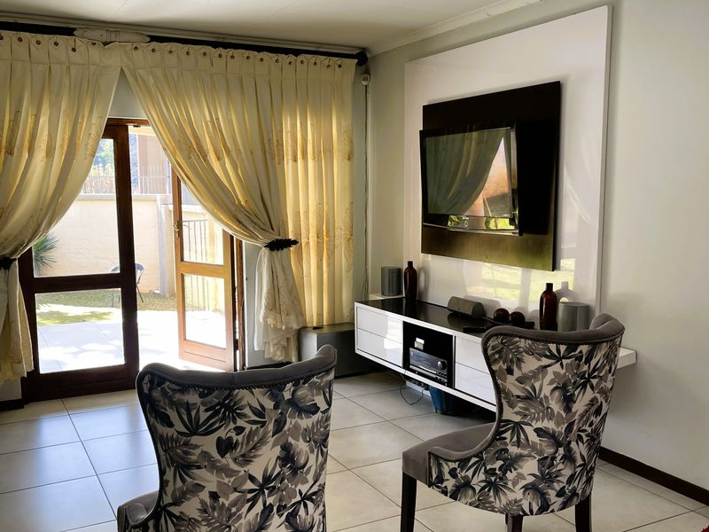 A bright living room featuring tiled flooring, a built-in media console, and direct access to an outdoor patio area through glass panel doors.
