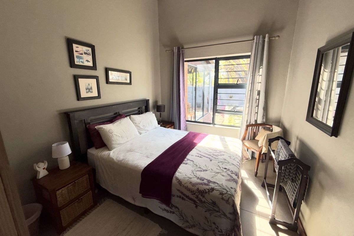 A well-lit bedroom featuring high ceilings, tiled flooring, and a large window providing natural light and views of the outdoor area.
