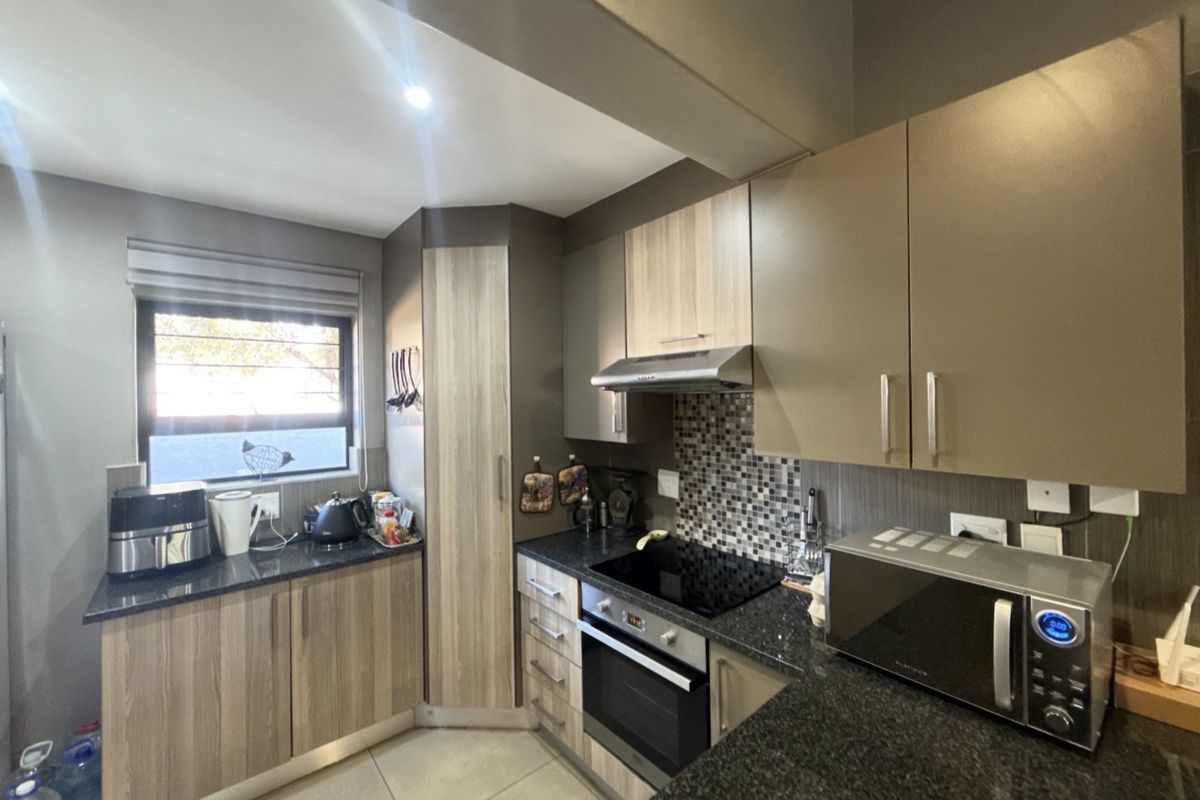 A modern kitchen featuring granite countertops, built-in oven, glass hob, extractor fan, and a mix of wood-grain and solid-tone cabinetry.