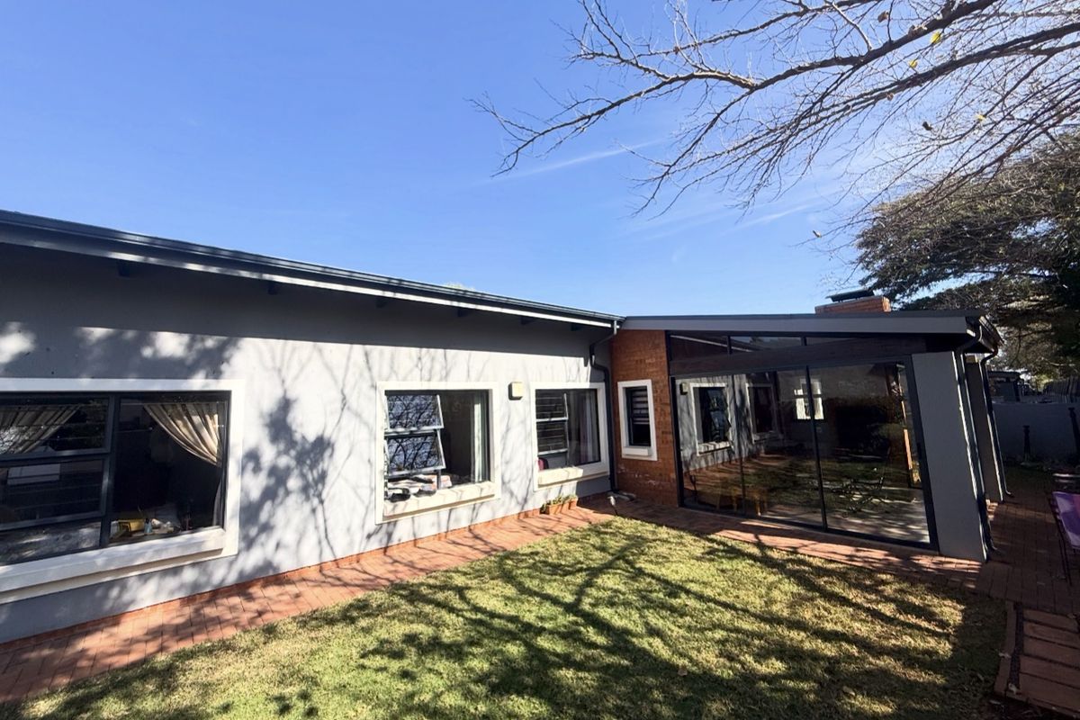 Rear view of the townhouse featuring a paved patio area, a small lawn, and a glass-enclosed sunroom extension with brick accents.