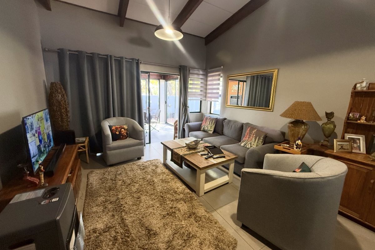 A comfortable living room featuring high vaulted ceilings with exposed timber beams, tiled flooring, and sliding glass doors providing access to an outdoor patio area.
