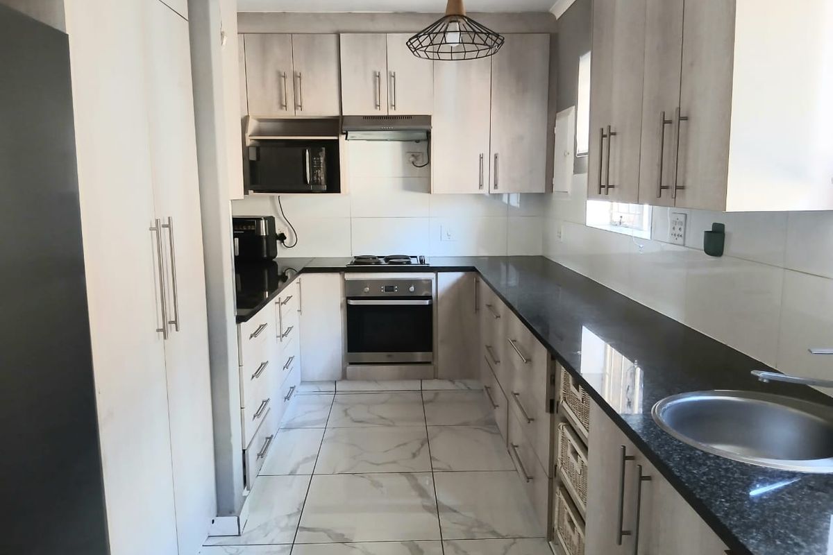 Modern U-shaped kitchen featuring light wood-grain cabinetry, contrasting black granite countertops, built-in oven, hob, extractor fan, and marble-look tiled flooring.