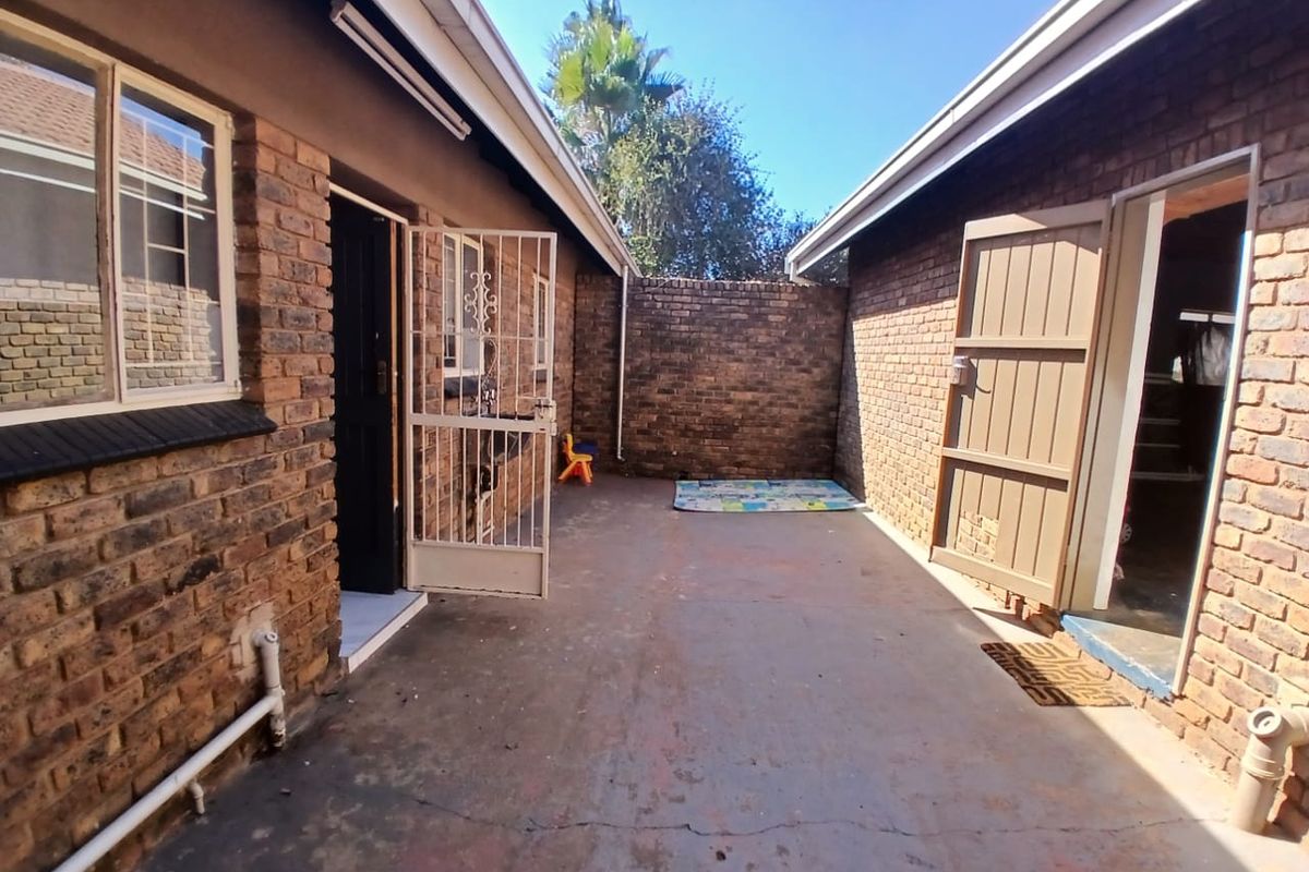 A private rear courtyard area featuring exposed brick walls, concrete flooring, and secure metal security gates providing access to the home.