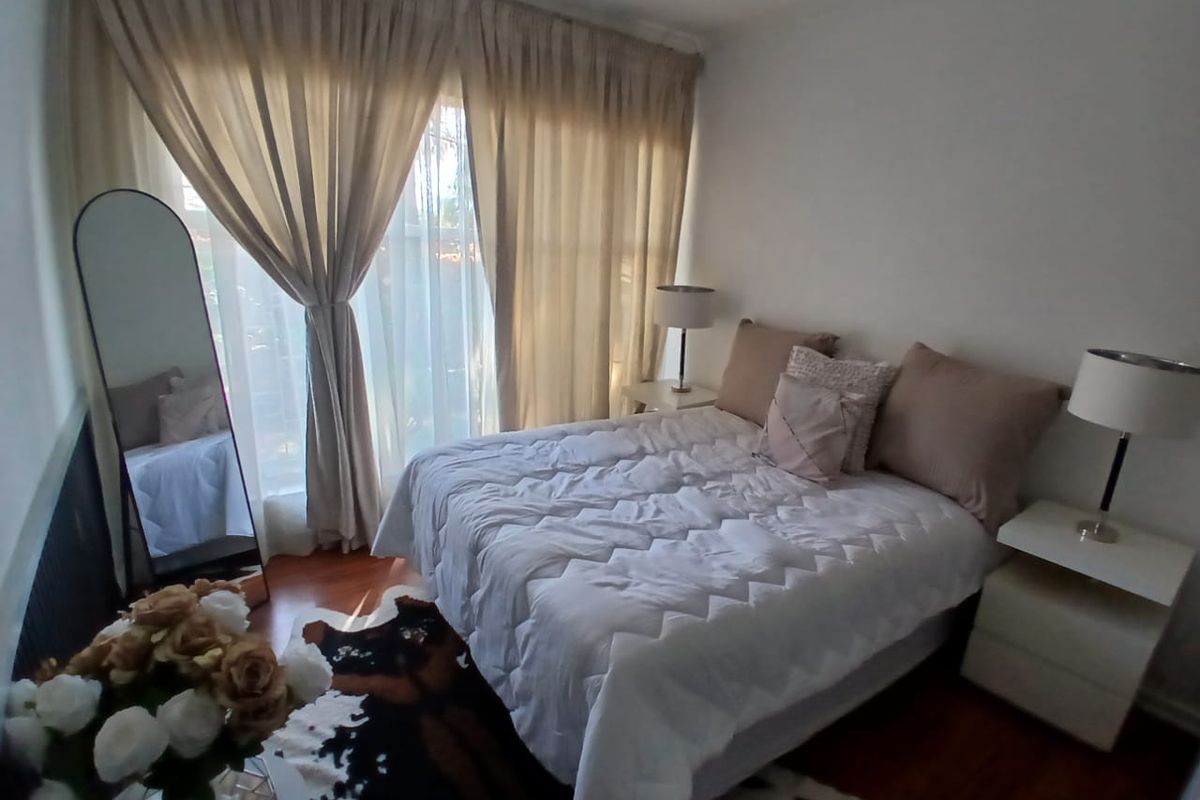 A well-lit bedroom featuring warm-toned wooden flooring and large floor-to-ceiling curtains providing natural light.