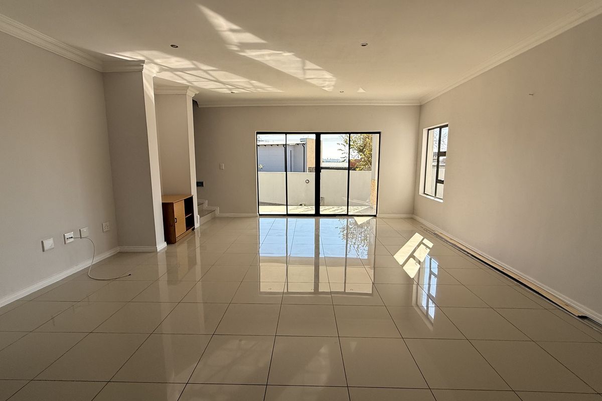 A spacious, empty living room featuring polished tile flooring, neutral walls, and large sliding glass doors providing natural light and access to the exterior.