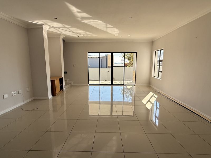 A spacious, empty living room featuring polished tile flooring, neutral walls, and large sliding glass doors providing natural light and access to the exterior.