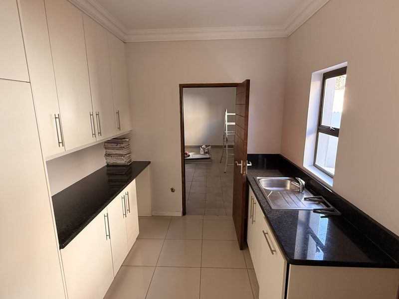 A clean and functional scullery featuring white built-in cabinetry, dark granite countertops, and a stainless steel sink with tiled flooring.