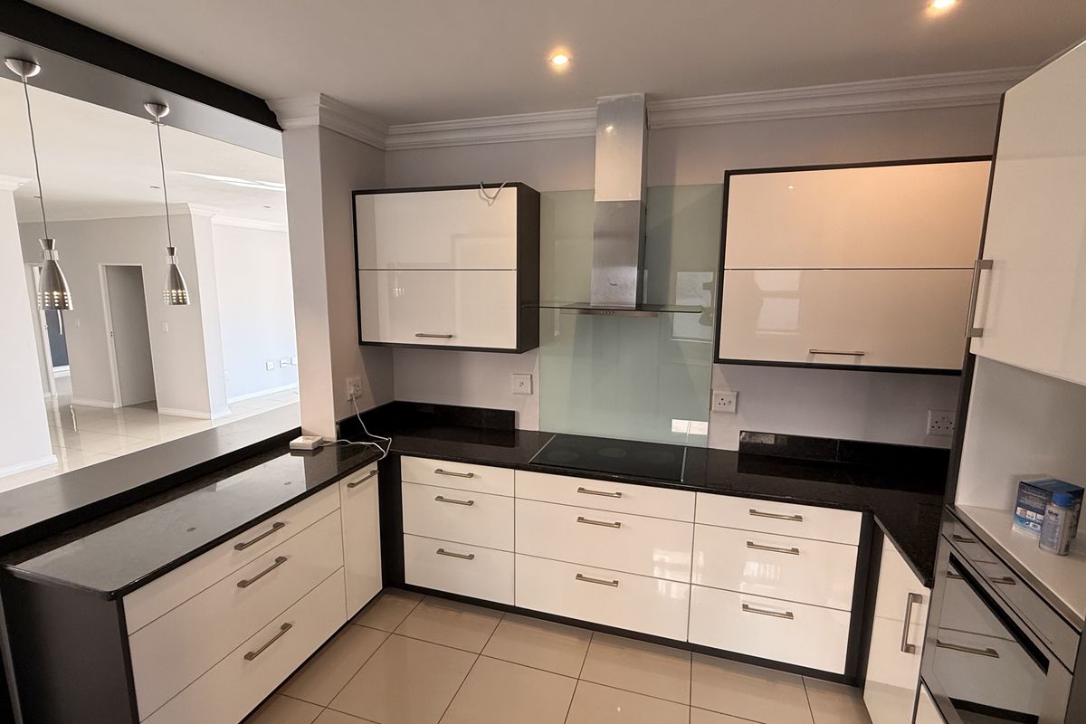 Modern kitchen featuring high-gloss cabinetry, granite countertops, integrated appliances, and a glass splashback, seamlessly connecting to the adjacent living area.