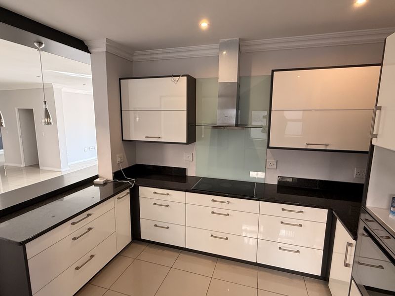 Modern kitchen featuring high-gloss cabinetry, granite countertops, integrated appliances, and a glass splashback, seamlessly connecting to the adjacent living area.