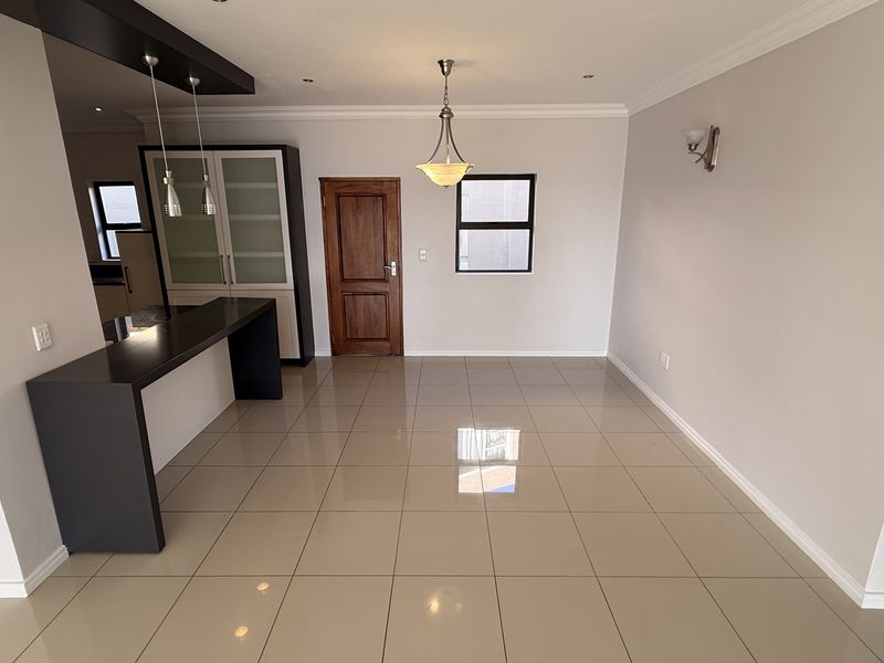 Spacious open-plan living area featuring polished porcelain floor tiles, a modern built-in breakfast bar, and elegant pendant lighting.
