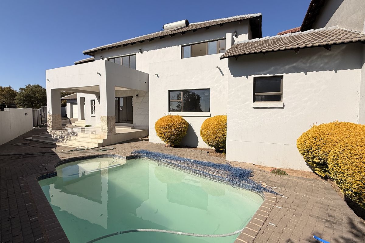 Rear exterior view of the house featuring a swimming pool, paved patio area, and a multi-level structure with a tiled roof.