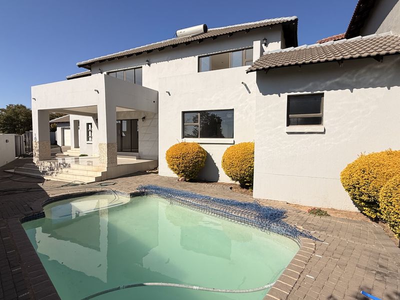 Rear exterior view of the house featuring a swimming pool, paved patio area, and a multi-level structure with a tiled roof.