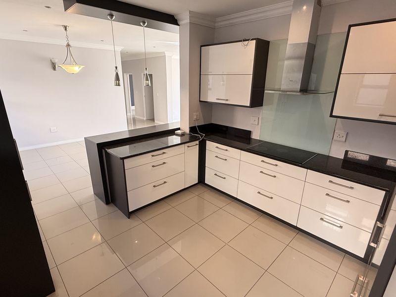 Modern open-plan kitchen featuring high-gloss cabinetry, stone countertops, integrated hob, and sleek glass splashback, flowing seamlessly into the adjacent living area.