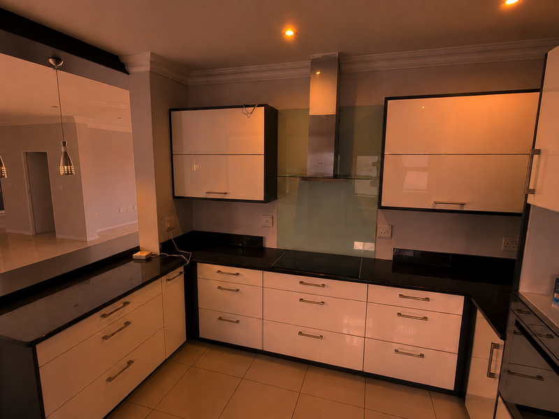 Modern kitchen featuring high-gloss cabinetry, granite countertops, integrated appliances, and a breakfast bar overlooking the open-plan living area.