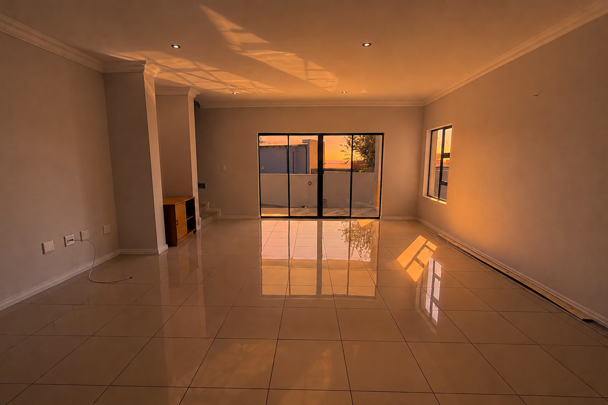A spacious, empty living area featuring polished tile flooring, recessed downlighting, and large sliding glass doors that provide access to the exterior.