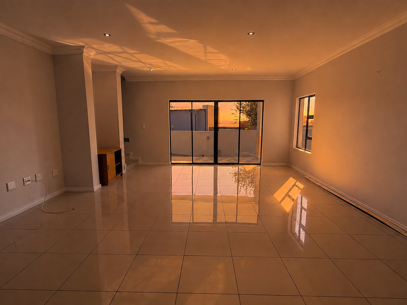 A spacious, empty living area featuring polished tile flooring, recessed downlighting, and large sliding glass doors that provide access to the exterior.