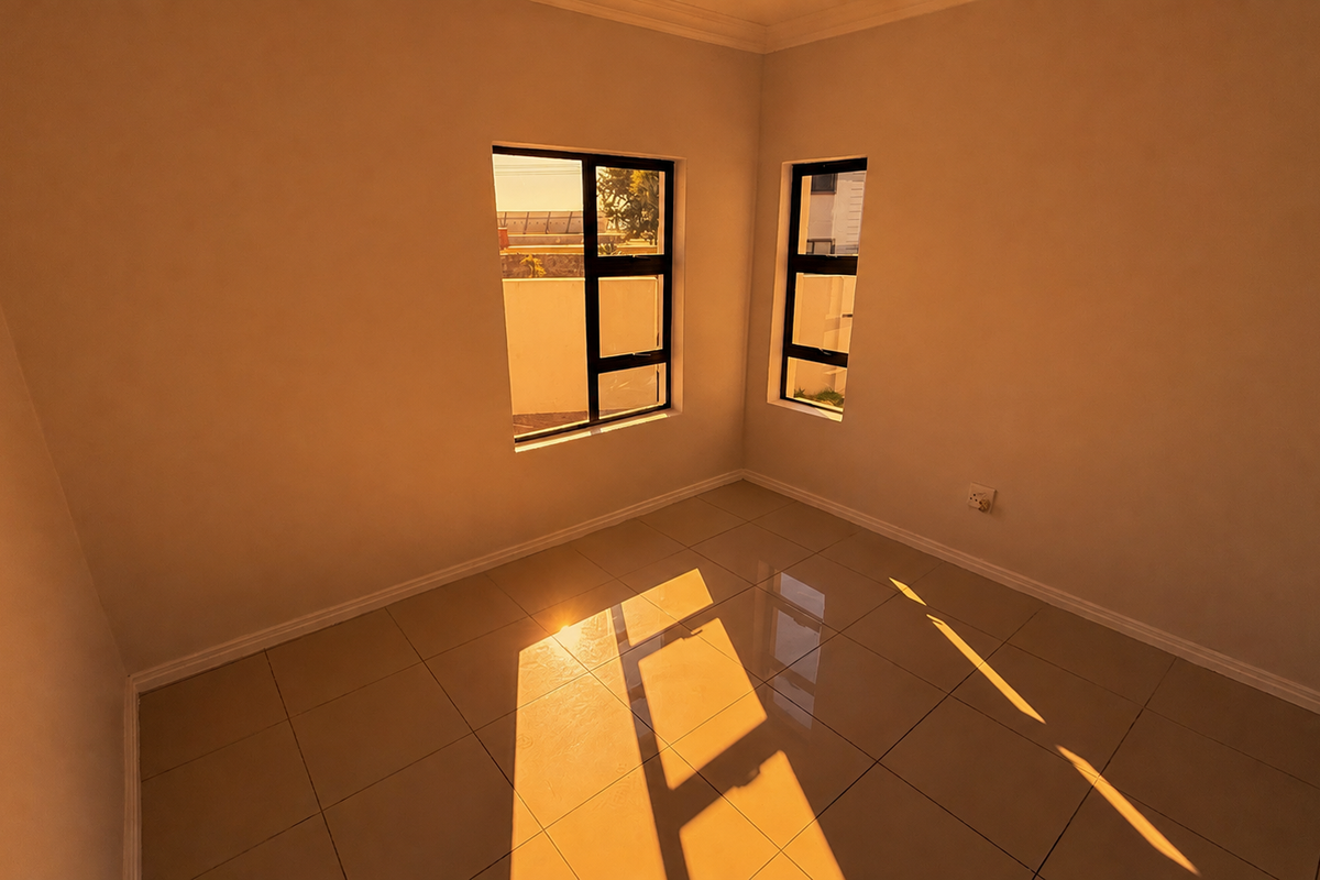 A bright, empty bedroom featuring neutral walls, polished floor tiles, and large aluminium-framed windows allowing for ample natural light.
