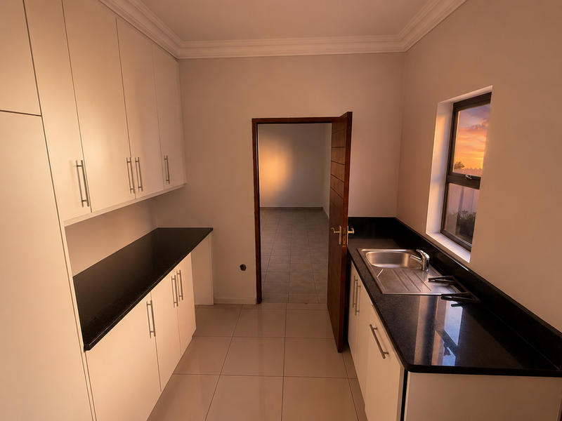 A clean, modern scullery featuring white built-in cabinetry, dark granite countertops, a stainless steel sink, and neutral tiled flooring.
