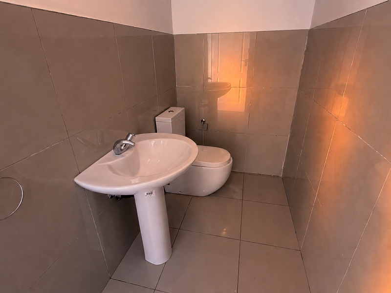A compact, fully tiled bathroom featuring a modern pedestal basin and toilet, presenting a clean and functional space.