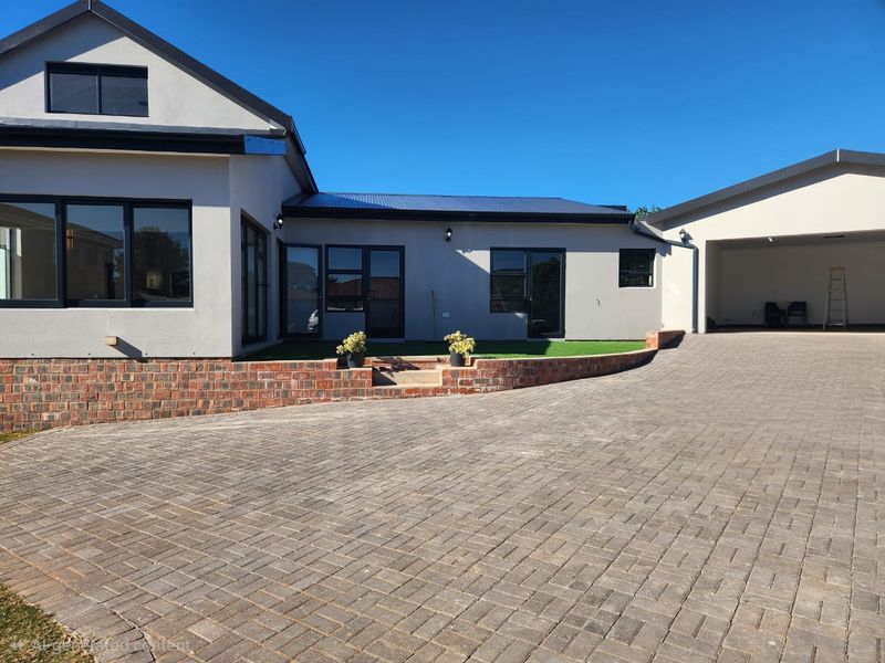 Modern residential exterior featuring a paved driveway, brick retaining wall, and an integrated double garage with clean architectural lines.
