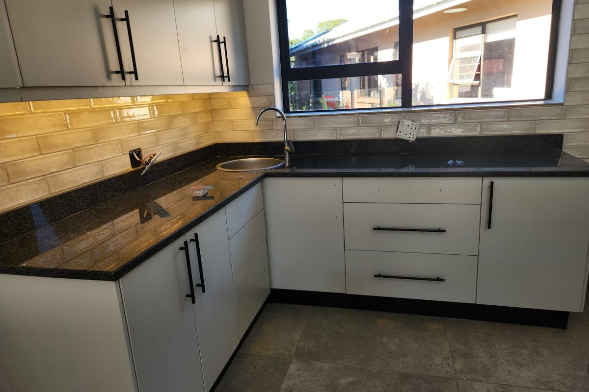 A modern kitchen featuring granite countertops, subway tile backsplash, and sleek cabinetry, currently awaiting final electrical finishing touches.