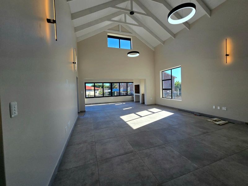 Spacious open-plan living area featuring a high vaulted ceiling with exposed rafters, large windows for natural light, and modern tiled flooring.