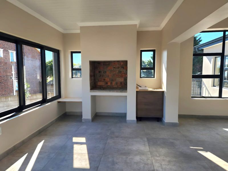 A bright, modern enclosed patio featuring large aluminium windows, tiled flooring, and a built-in brick braai, offering a versatile space for indoor-outdoor entertaining.