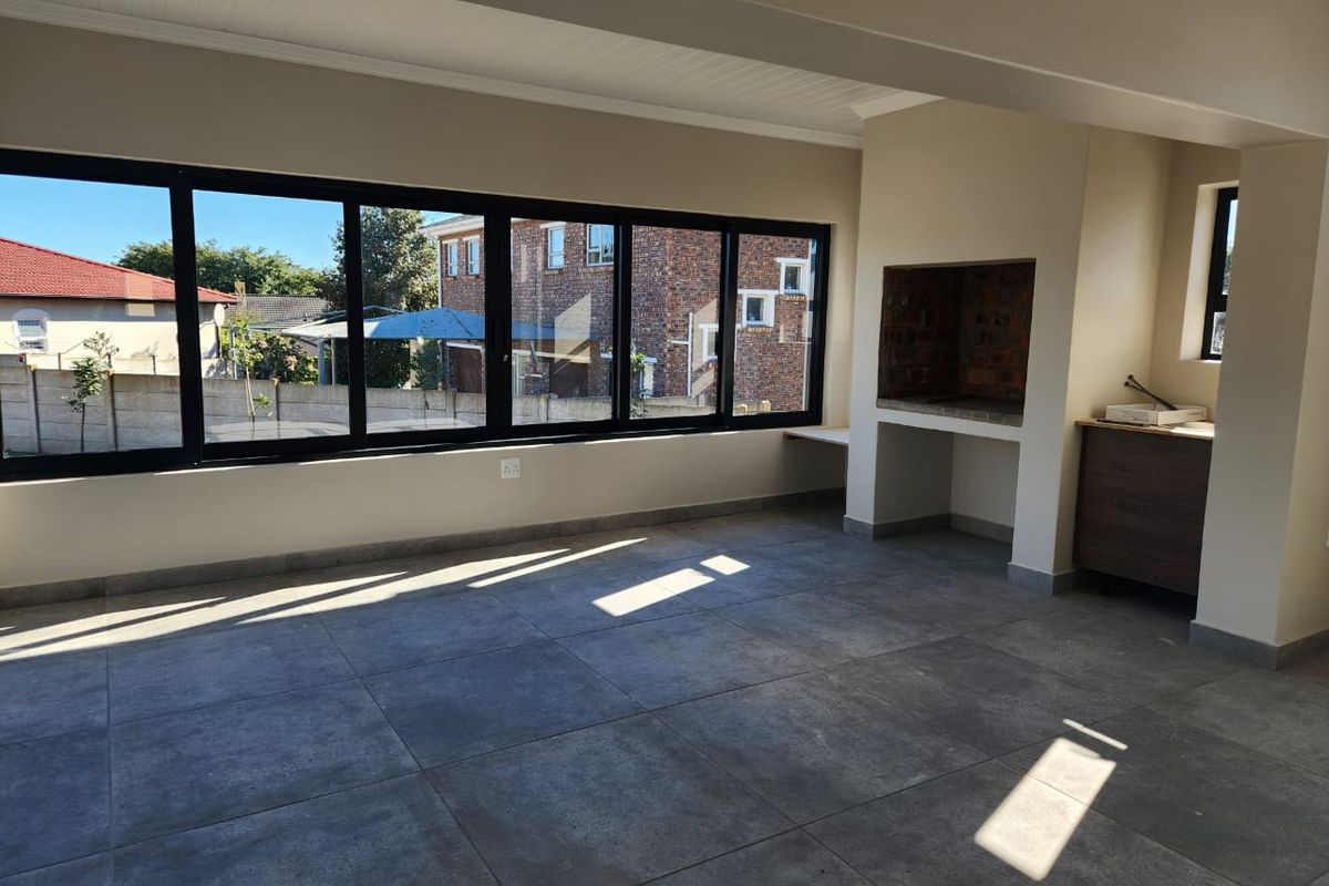 Spacious living area featuring large windows, tiled flooring, and a built-in indoor braai, offering a bright and versatile space for entertaining.