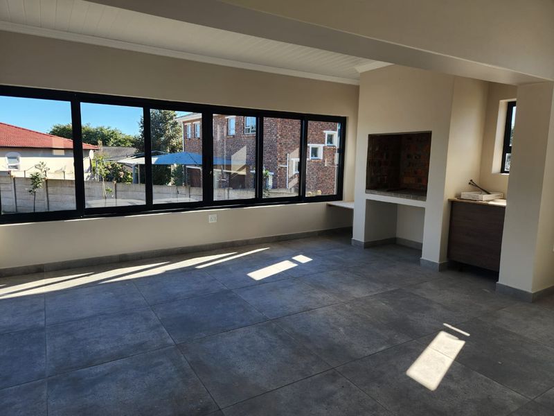 Spacious living area featuring large windows, tiled flooring, and a built-in indoor braai, offering a bright and versatile space for entertaining.