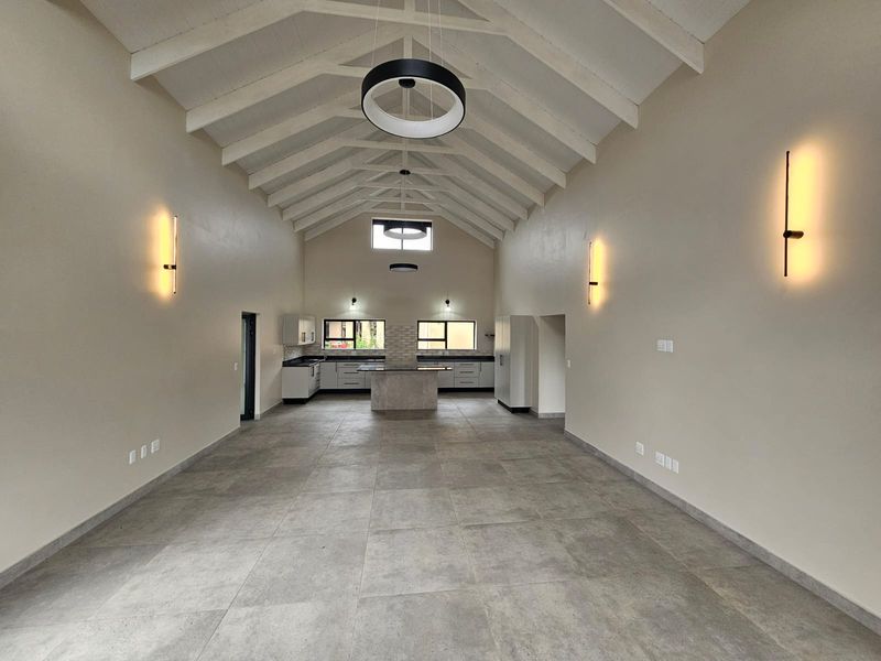 Spacious open-plan living and kitchen area featuring a high vaulted ceiling with exposed rafters, modern tiled flooring, and contemporary lighting fixtures.