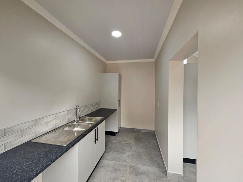 A clean, modern scullery featuring a stainless steel double sink, dark laminate countertops, subway tile backsplash, and ample built-in cabinetry.