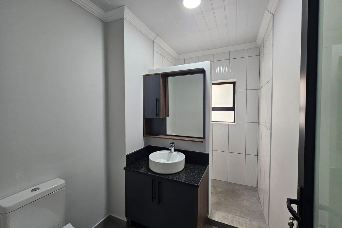 A modern, clean bathroom featuring a dark vanity with a vessel sink, granite countertop, and a separate tiled shower area.