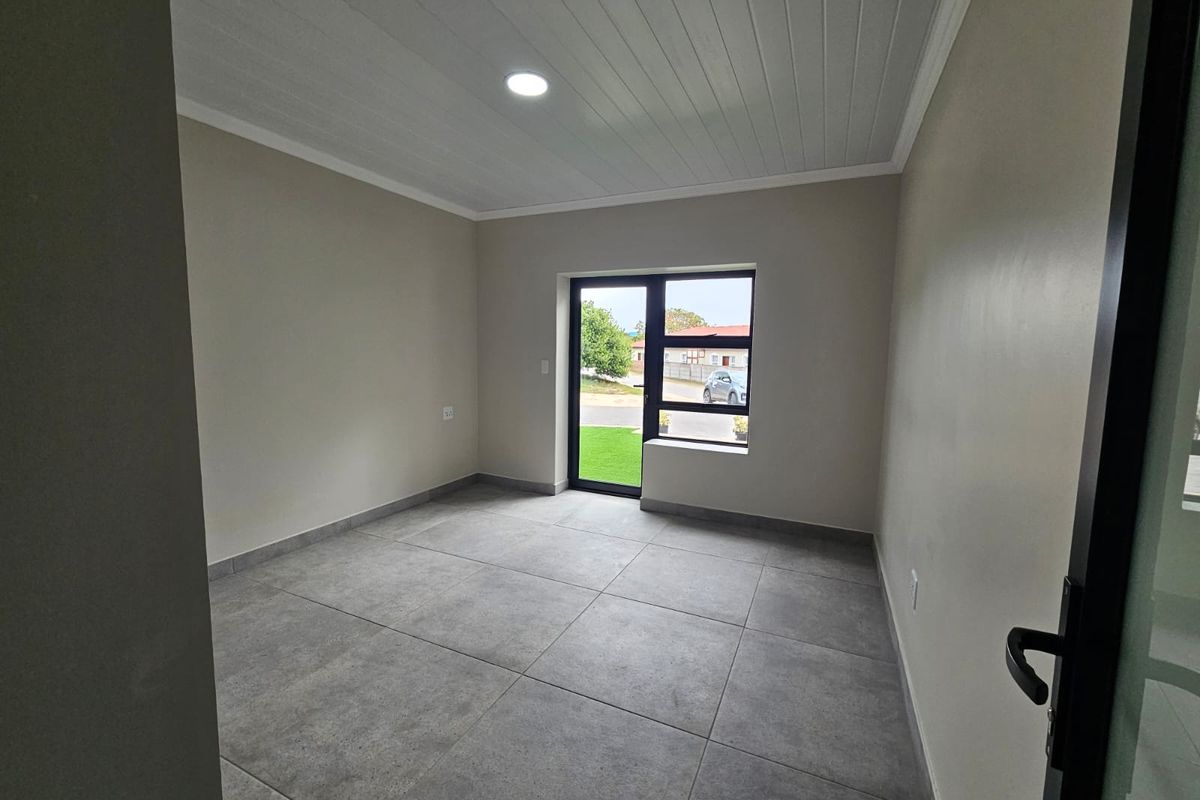 A bright, empty bedroom featuring modern large-format floor tiles, a clean tongue and groove ceiling, and a large aluminium-framed window and door.