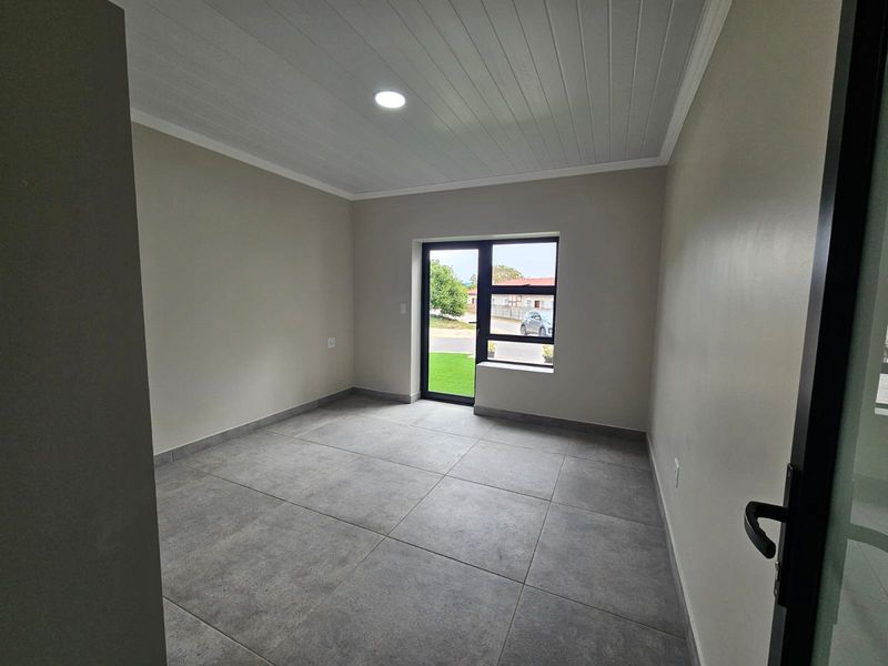 A bright, empty bedroom featuring modern large-format floor tiles, a clean tongue and groove ceiling, and a large aluminium-framed window and door.