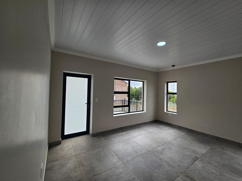 A bright, modern, and empty living space featuring large windows, tiled flooring, and a clean tongue and groove ceiling finish.