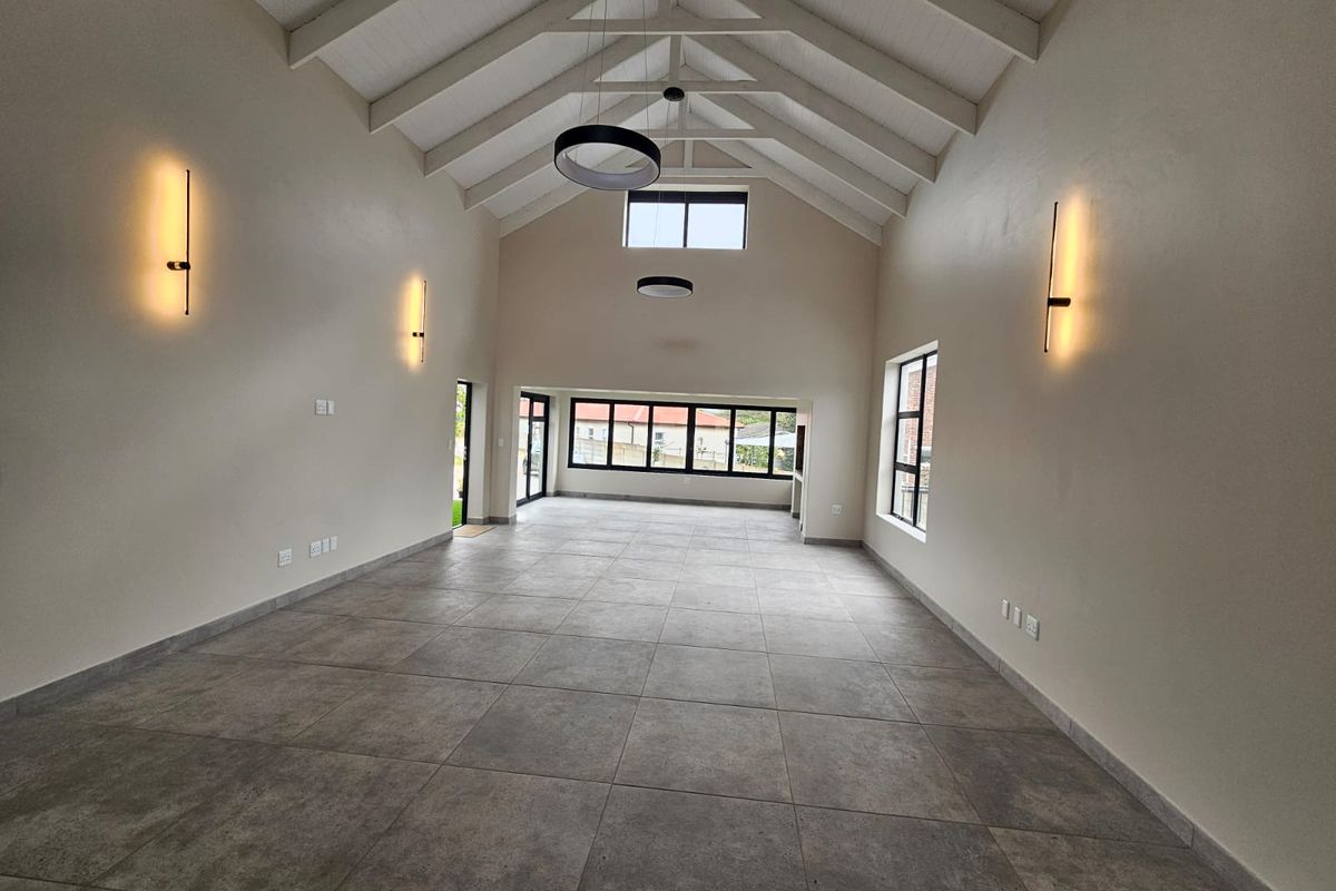 Spacious, light-filled living area featuring a high vaulted ceiling with exposed rafters, modern tiled flooring, and large windows providing ample natural light.