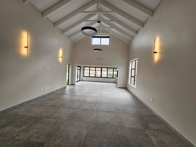 Spacious, light-filled living area featuring a high vaulted ceiling with exposed rafters, modern tiled flooring, and large windows providing ample natural light.