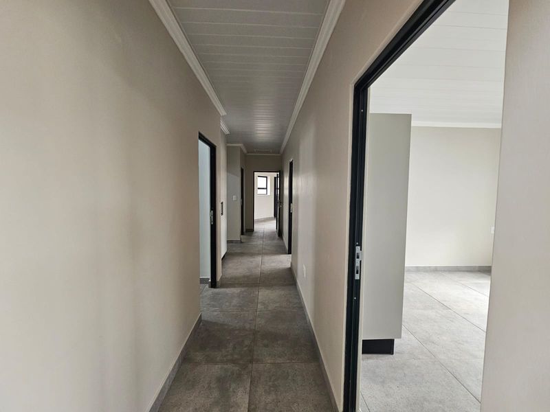 A clean, neutral hallway featuring large format floor tiles, coved ceilings, and multiple doorways leading to adjacent rooms.