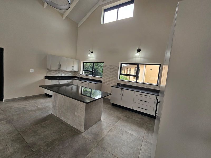 Modern, spacious kitchen featuring a central island, granite countertops, ample cabinetry, tiled flooring, and a high vaulted ceiling with natural light.