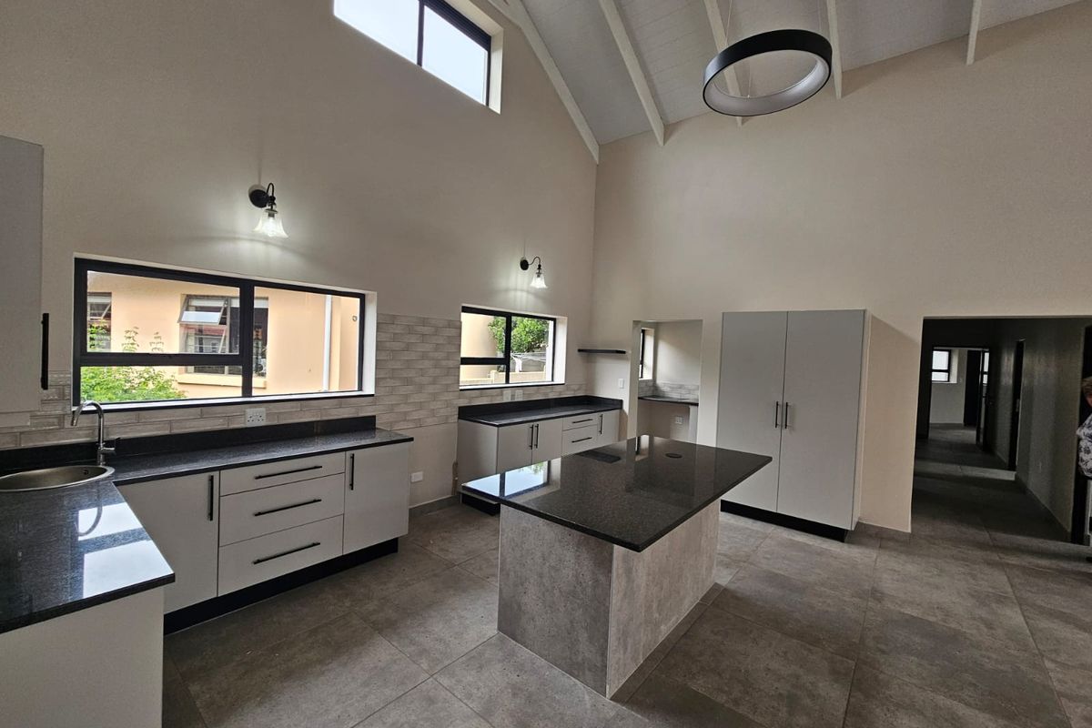 Modern, spacious kitchen featuring a central island, granite countertops, sleek cabinetry, vaulted ceilings, and abundant natural light from clerestory windows.
