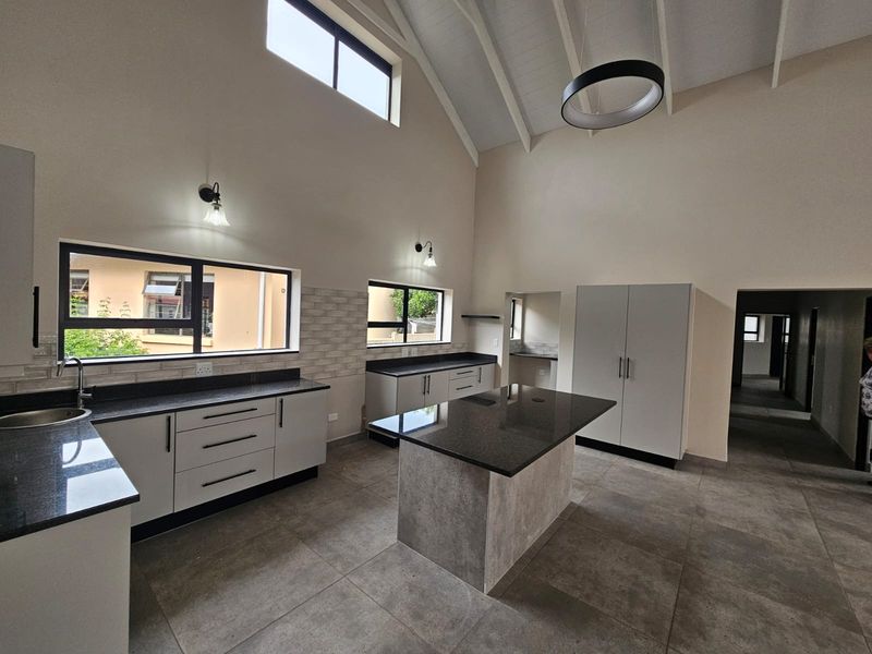 Modern, spacious kitchen featuring a central island, granite countertops, sleek cabinetry, vaulted ceilings, and abundant natural light from clerestory windows.