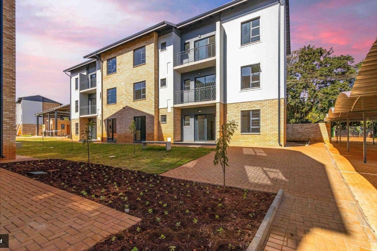 A modern multi-story apartment building featuring brick and plaster facade, private balconies, paved walkways, and landscaped garden areas.