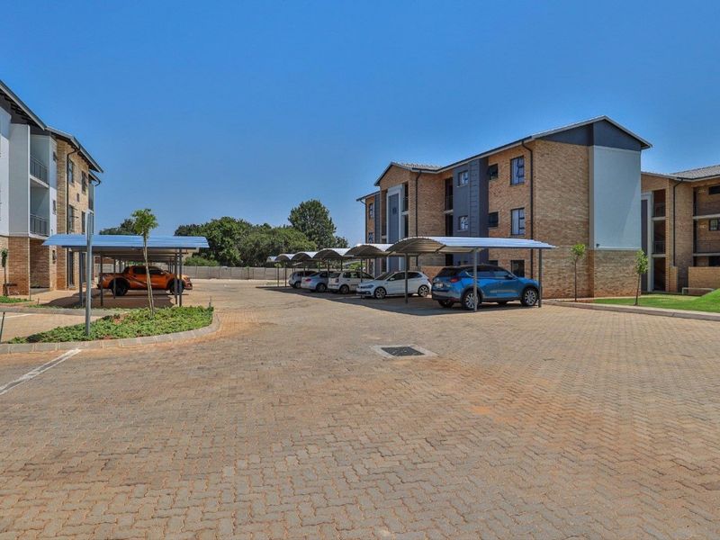 Exterior view of an apartment complex featuring paved parking areas with covered carports and modern brick and plaster building facades.