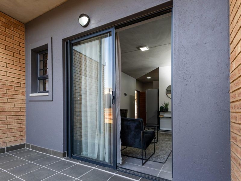 A modern covered patio featuring tiled flooring, face brick accents, and a large sliding glass door providing access to the interior living space.